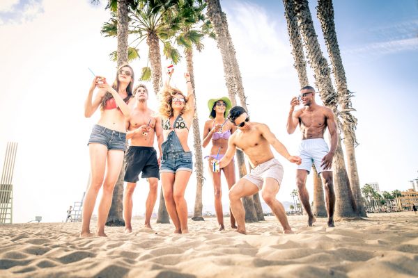 Group of friends having party on the beach, dancing and drinking cocktails